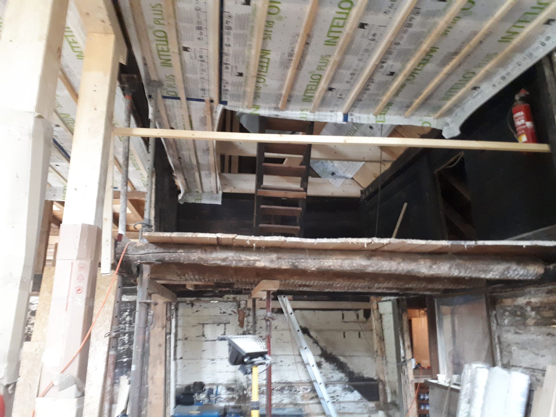 Innenansicht einer Baustelle mit freiliegenden Balken, einer teilweise errichteten Decke und einer kleinen Holztreppe.