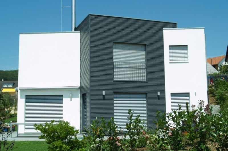 Modernes zweistöckiges Haus mit weiß-grauer Fassade, Rollläden und einem grünen Garten.