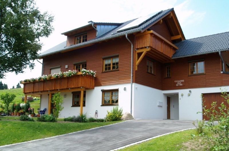 Zweistöckiges, braun-weißes Haus mit Balkon und Solaranlage auf einem grünen Rasen mit Einfahrt.