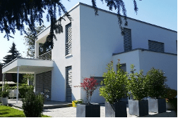 Modernes weißes zweistöckiges Haus mit Flachdach, Terrasse und quadratischen Pflanzkästen mit Grünpflanzen.