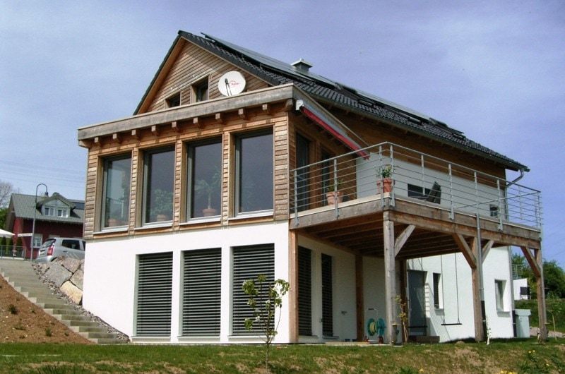 Modernes zweistöckiges Haus mit Holz- und weißer Fassadenverkleidung, Solaranlage, Balkon und großen Fenstern.