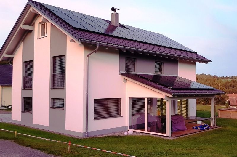 Modernes zweistöckiges Haus mit Solarpaneelen auf dem Dach und Veranda, eingebettet in einen Rasengarten.