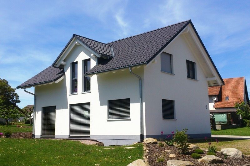 Weißes Haus mit schwarzem Dach, zwei Stockwerke, mit einem grasbewachsenen Rasen an einem sonnigen Tag.