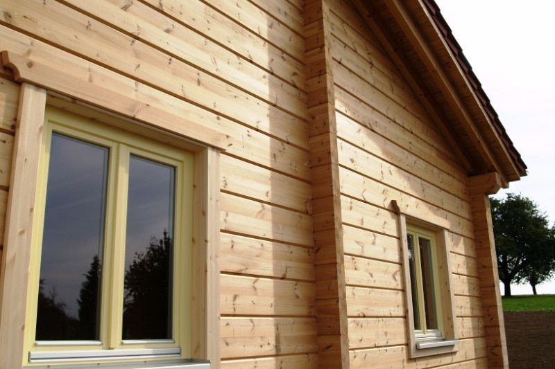 Holzhausfassade mit zwei Fenstern und Dachlinie, durchflutet von natürlichem Licht.