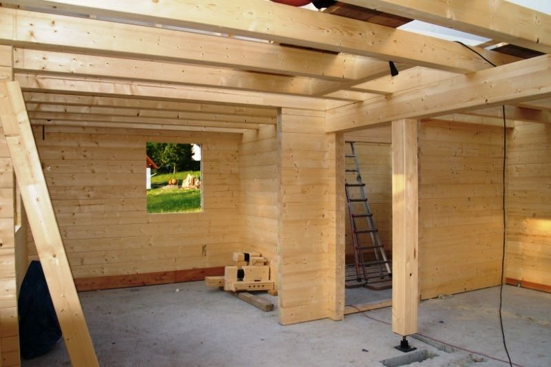 Innenansicht einer im Bau befindlichen Holzkonstruktion mit Betonboden, Fenster und Leiter.