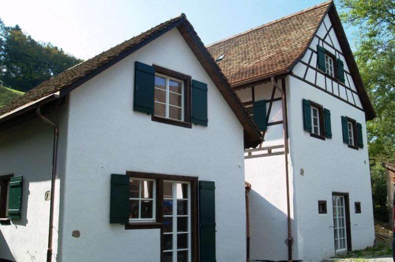 Zweistöckige weiße Gebäude mit braunen Dächern, grünen Fensterläden und Fachwerkkonstruktion.