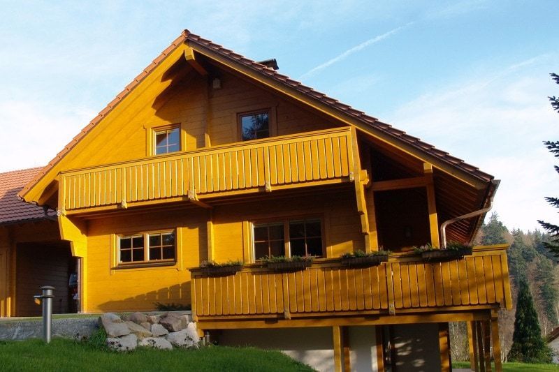 Ein Holzhaus mit Balkon vor blauem Himmel, das die natürlichen Farbtöne des Holzes zur Geltung bringt.
