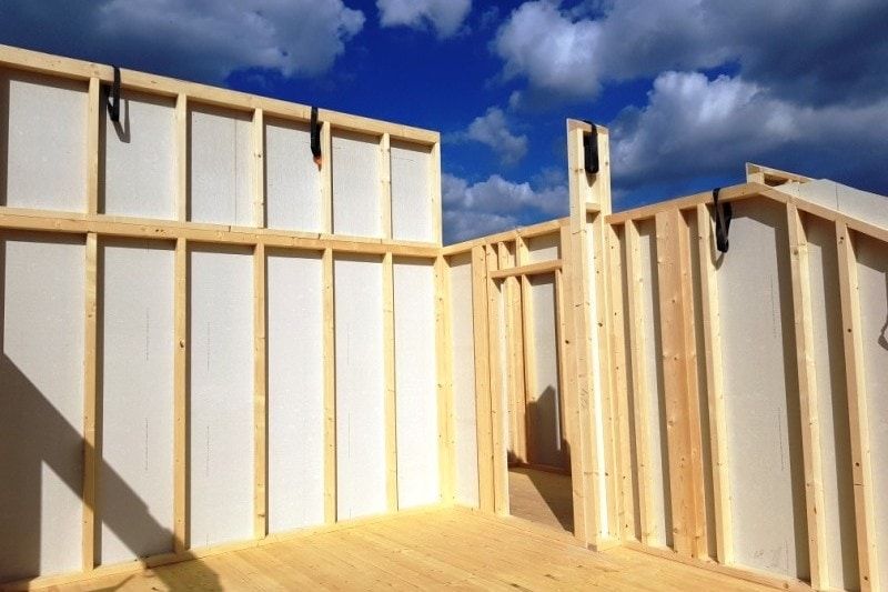 Innenansicht eines Holzrahmenhauses mit isolierten Wänden und Boden vor blauem Himmel.