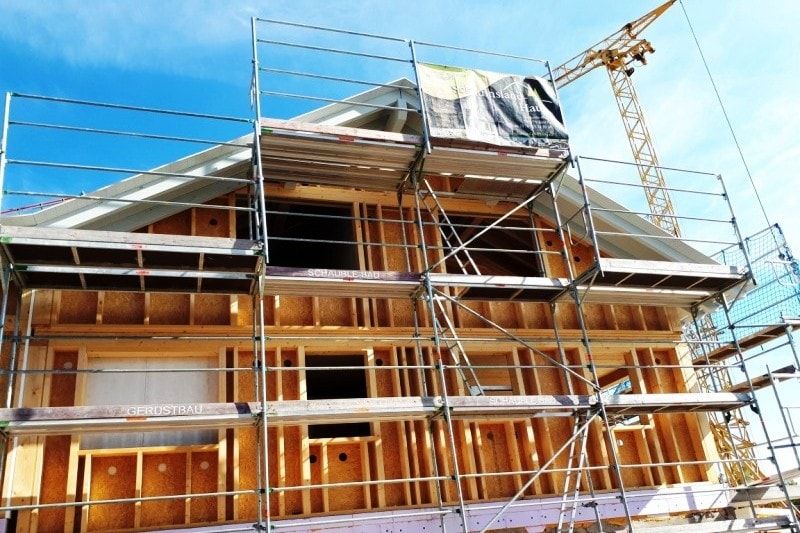 Ein im Bau befindliches Holzhaus mit Gerüst und Kran vor blauem Himmel.