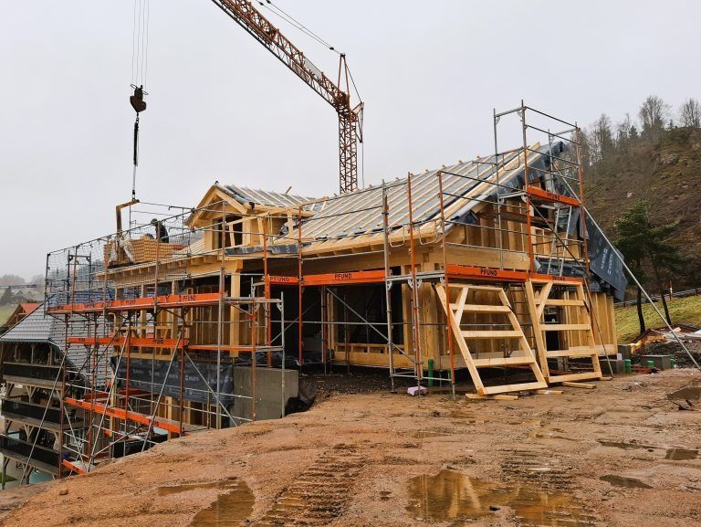 Errichtung eines Holzhauses mit Gerüst, Kran und unfertigem Dach auf einer schlammigen Baustelle.