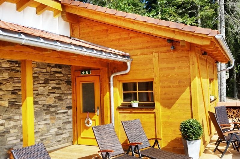 Saunagebäude aus Holz mit Sonnenliegen auf einer Terrasse, Fassade aus braunem Holz und Stein.