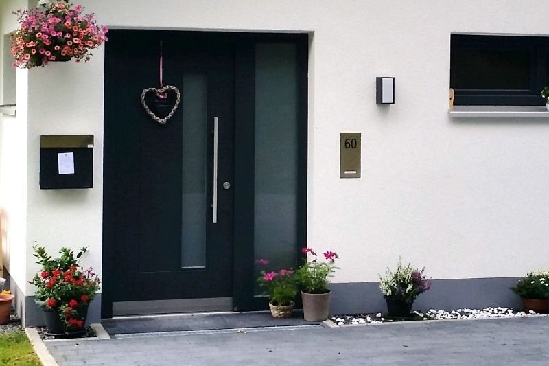 Dunkle Haustür mit Glasscheibe, Herzverzierung und Topfblumen.