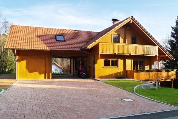 Holzhaus mit überdachtem Carport, rotem Ziegeldach und gemauerter Auffahrt.