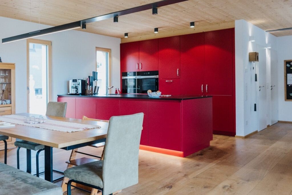 Moderne Küche mit roten Schränken, Kochinsel, Holzdecke und -boden sowie einem Esstisch.