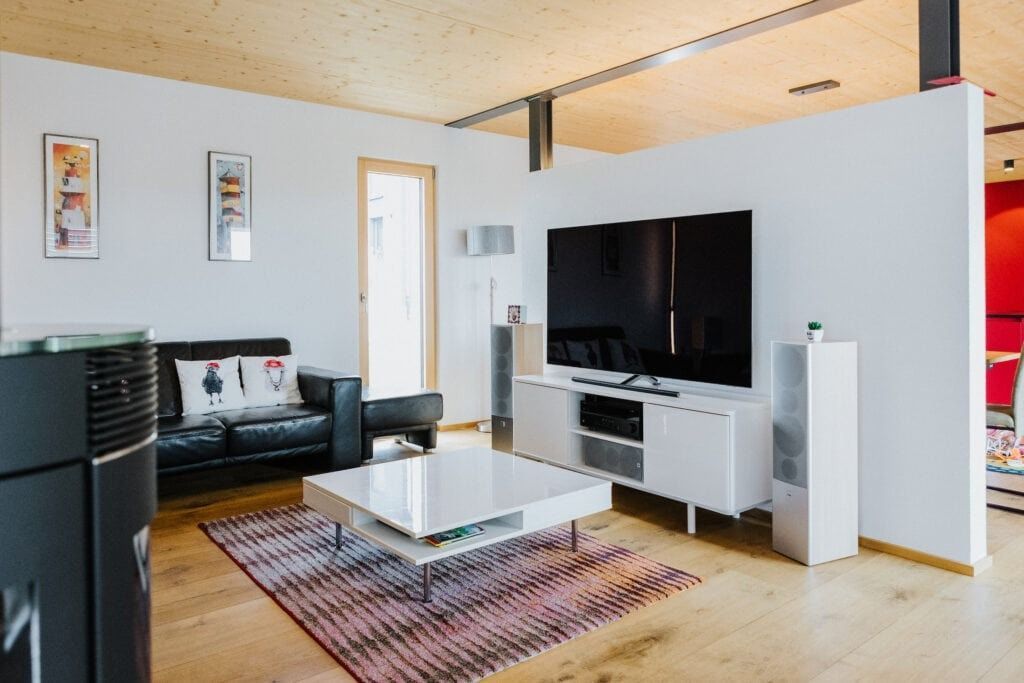 Modernes Wohnzimmer mit schwarzem Ledersofa, weißem Fernsehschrank, Holzboden und einem großen Fernseher.