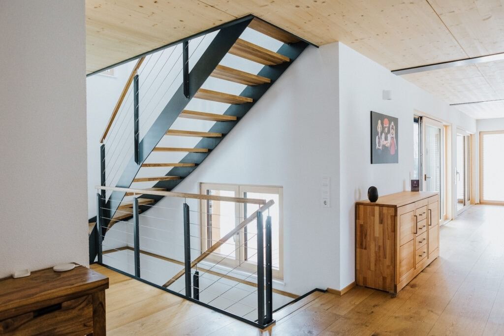 Holztreppe mit schwarzem Metallgeländer in einem modernen, lichtdurchfluteten Interieur.