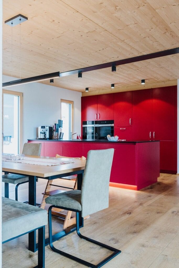 Moderne Küche mit roter Kochinsel und Schränken, Holzdecke und -boden, Tisch mit Stühlen.