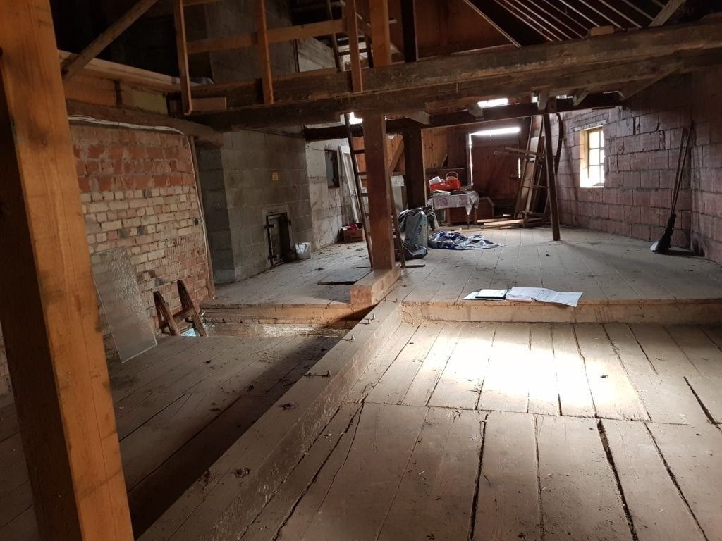 Im Bau befindlicher, mit Holzboden ausgestatteter Dachboden; freiliegende Balken, Ziegelwände und natürliches Licht.