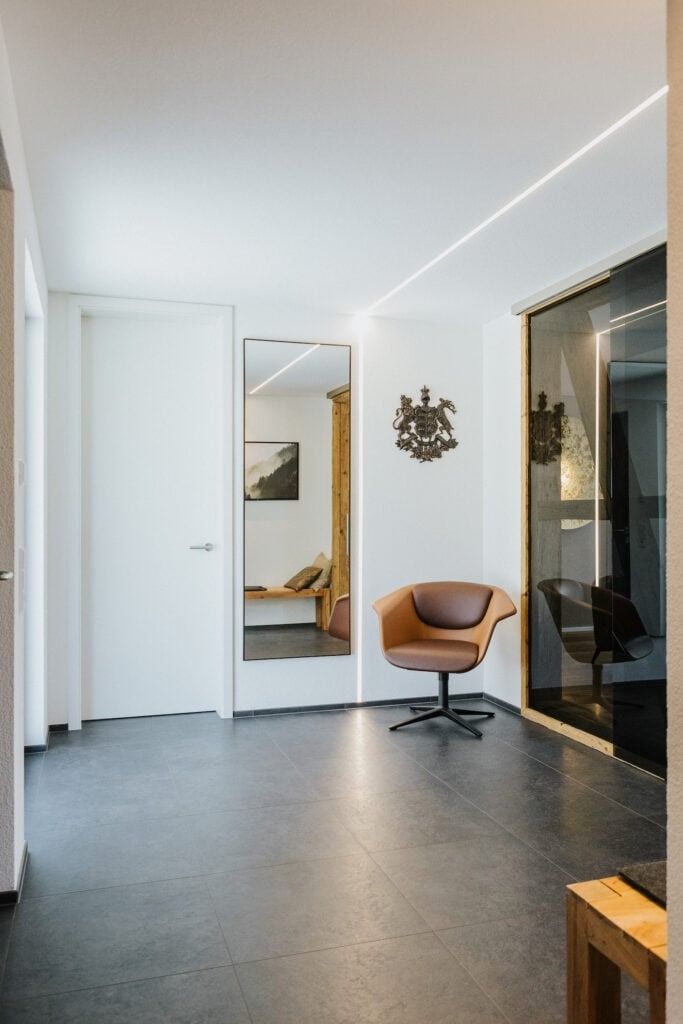 Flur in modernem Design; weiße Wände, grauer Boden, brauner Sessel und großer Spiegel.