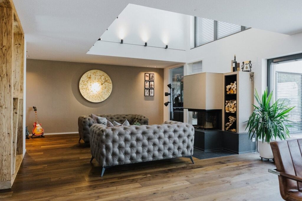 Wohnzimmer mit gestepptem grauen Sofa, Kamin und Dachfenster. Holzböden und -wände.