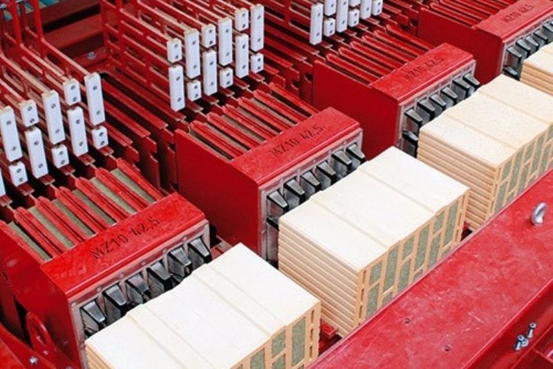 Industriemaschine in Rot und Beige mit gestapelten Bauteilen und Metallverbindern.