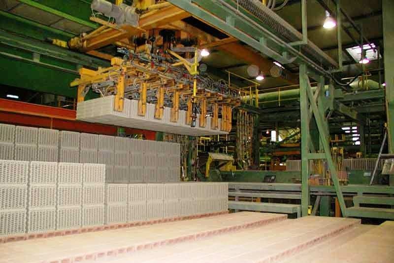 Ein Roboterarm hebt in einer Fabrikumgebung Betonblöcke von oben an.