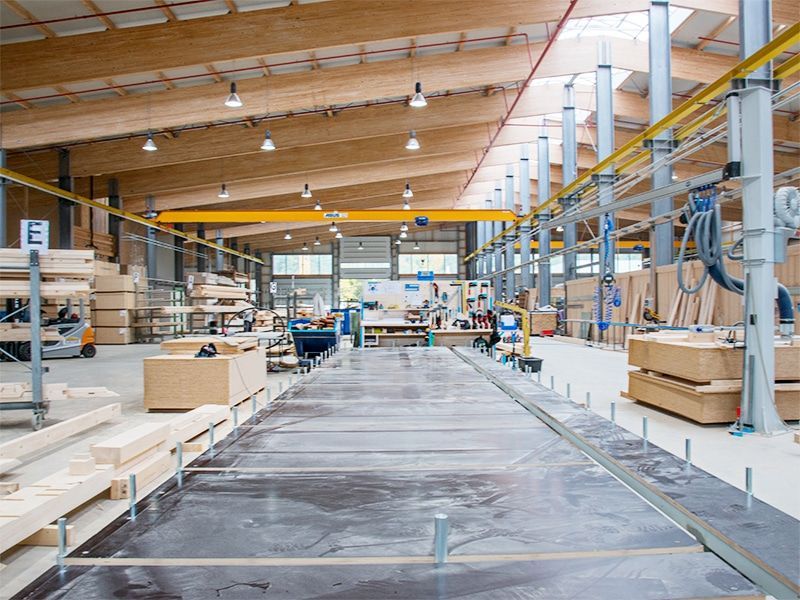 Innenansicht einer Fabrik aus Holz mit Holzbalken, Maschinen und gestapelten Materialien.