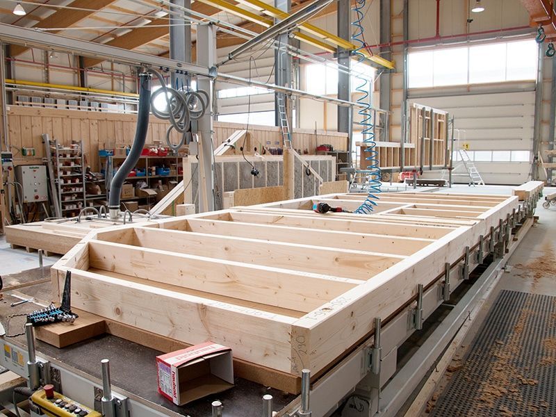 Im Inneren einer Fabrik, in der Maschinen und Materialien gelagert werden, entsteht ein Holzrahmen für den Fußboden eines Hauses.