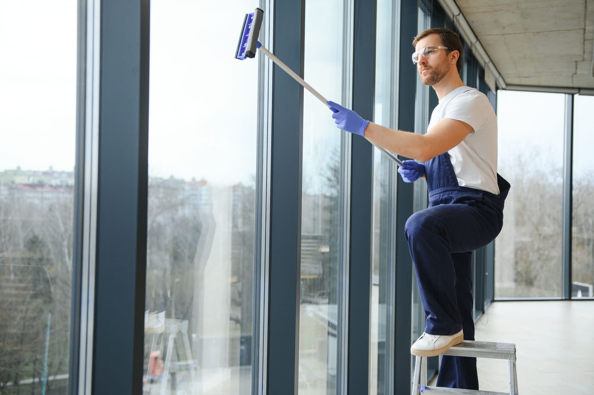Persona limpiando ventanas altas con una rasqueta en una oficina luminosa.
