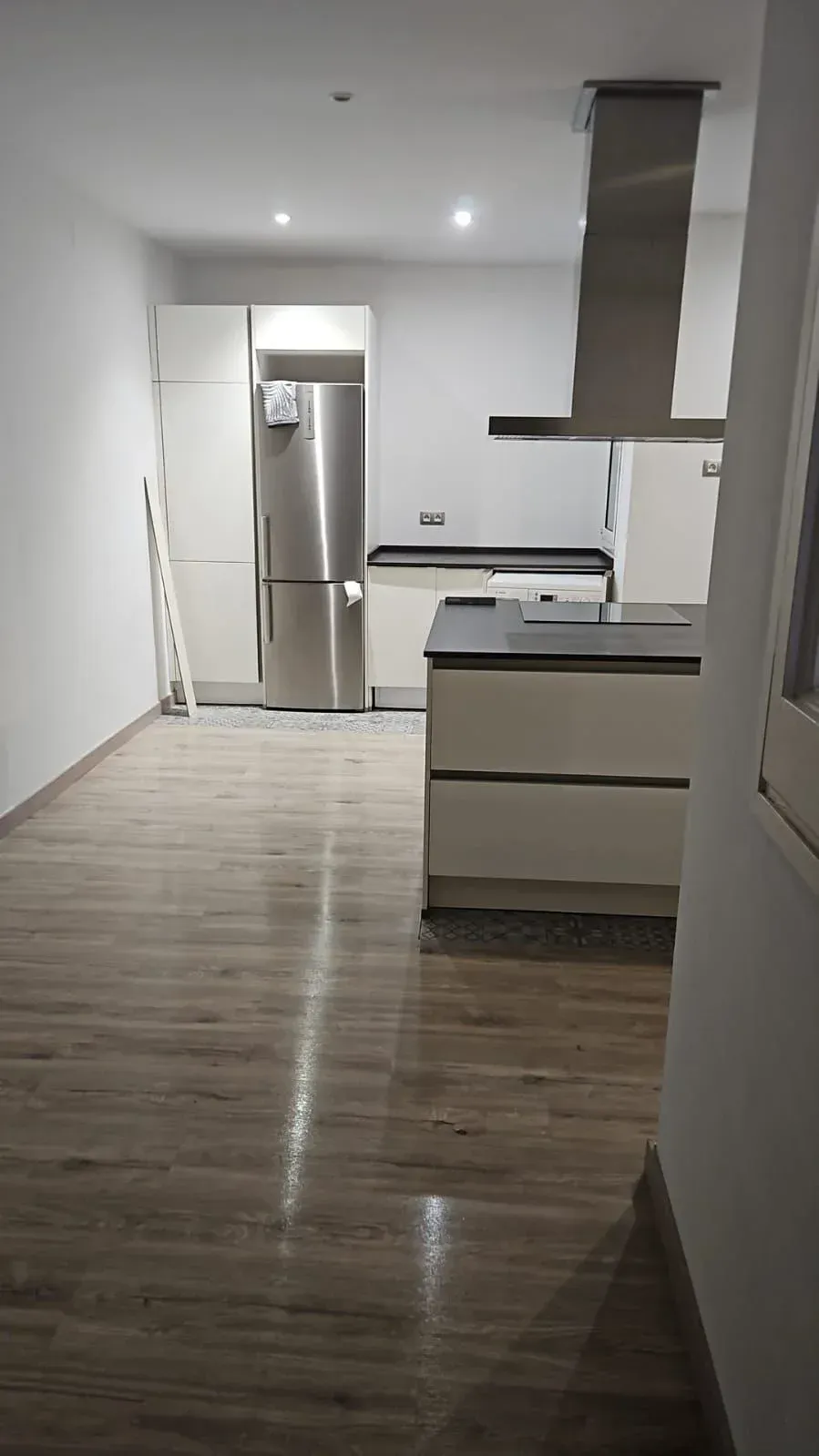 Cocina moderna con refrigerador de acero inoxidable, isla, gabinetes claros y pisos símil madera.