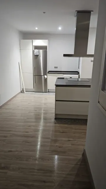 Cocina moderna con refrigerador de acero inoxidable, isla, gabinetes claros y pisos símil madera.