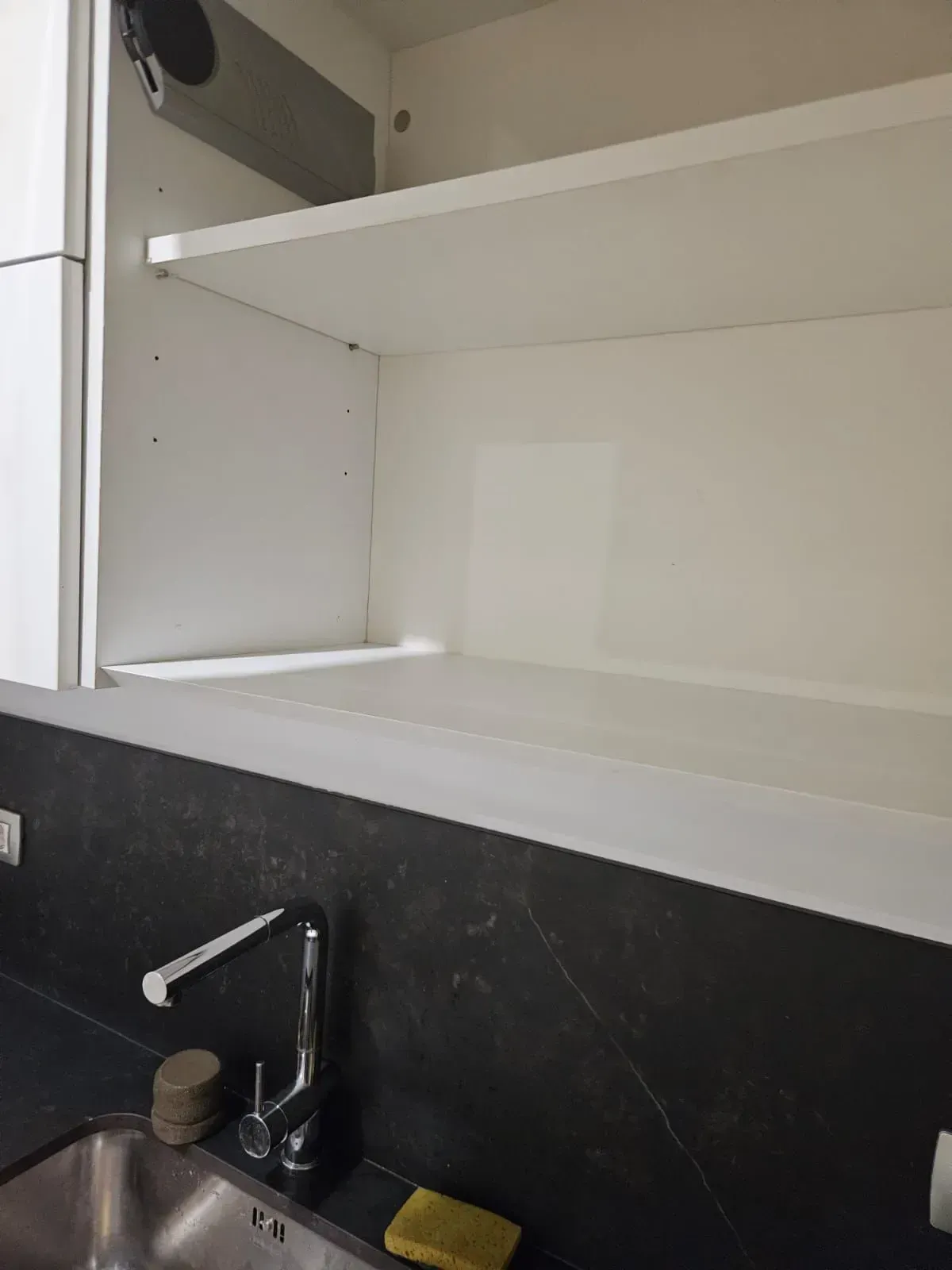 Mueble de cocina blanco vacío con un estante sobre un fregadero y protector contra salpicaduras oscuro.