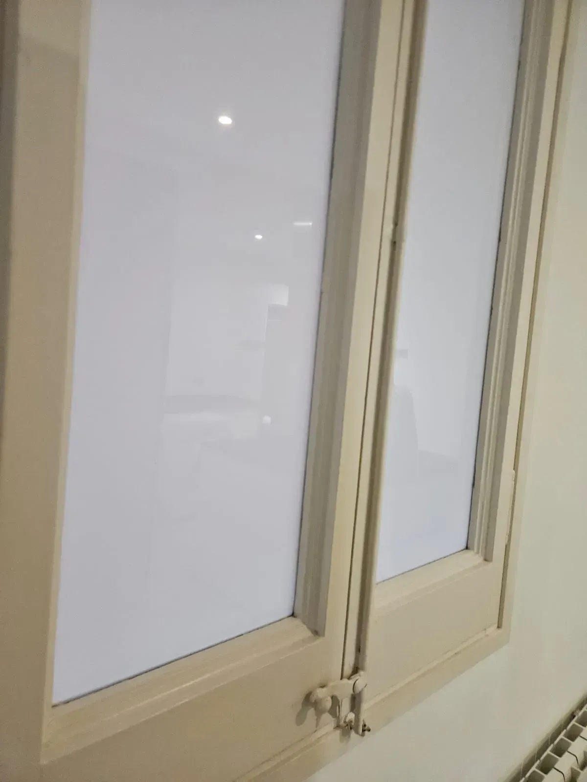 Dos paneles de ventana de color blanco roto, cerrados, con vidrio reflectante, colocados en un marco beige claro