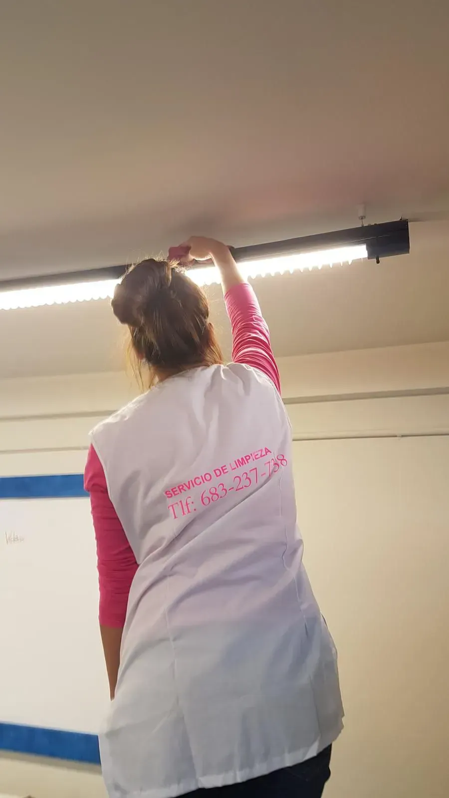 Una mujer con un chaleco blanco y un texto en la espalda se acerca a las luces del techo.