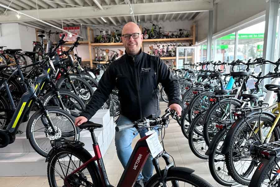 Ein Mann steht in einem Fahrradladen neben einem Elektrofahrrad.