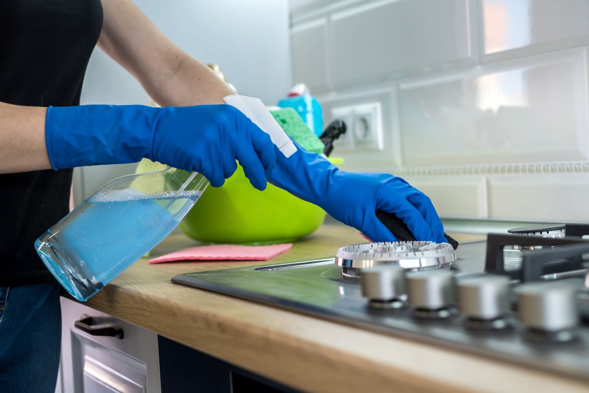 Mains gantées vaporisant et essuyant une plaque de cuisson avec un produit nettoyant et un chiffon.