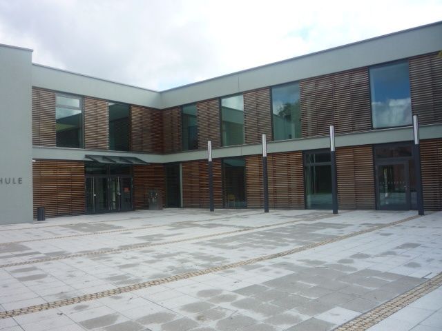 Modernes Gebäude mit Holzvertäfelung und großen Fenstern in einem gepflasterten Innenhof.