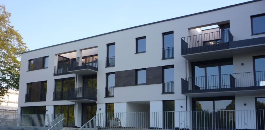 Modernes Mehrfamilienhaus mit Balkonen, grau-weißer Fassade, Metallgeländer.