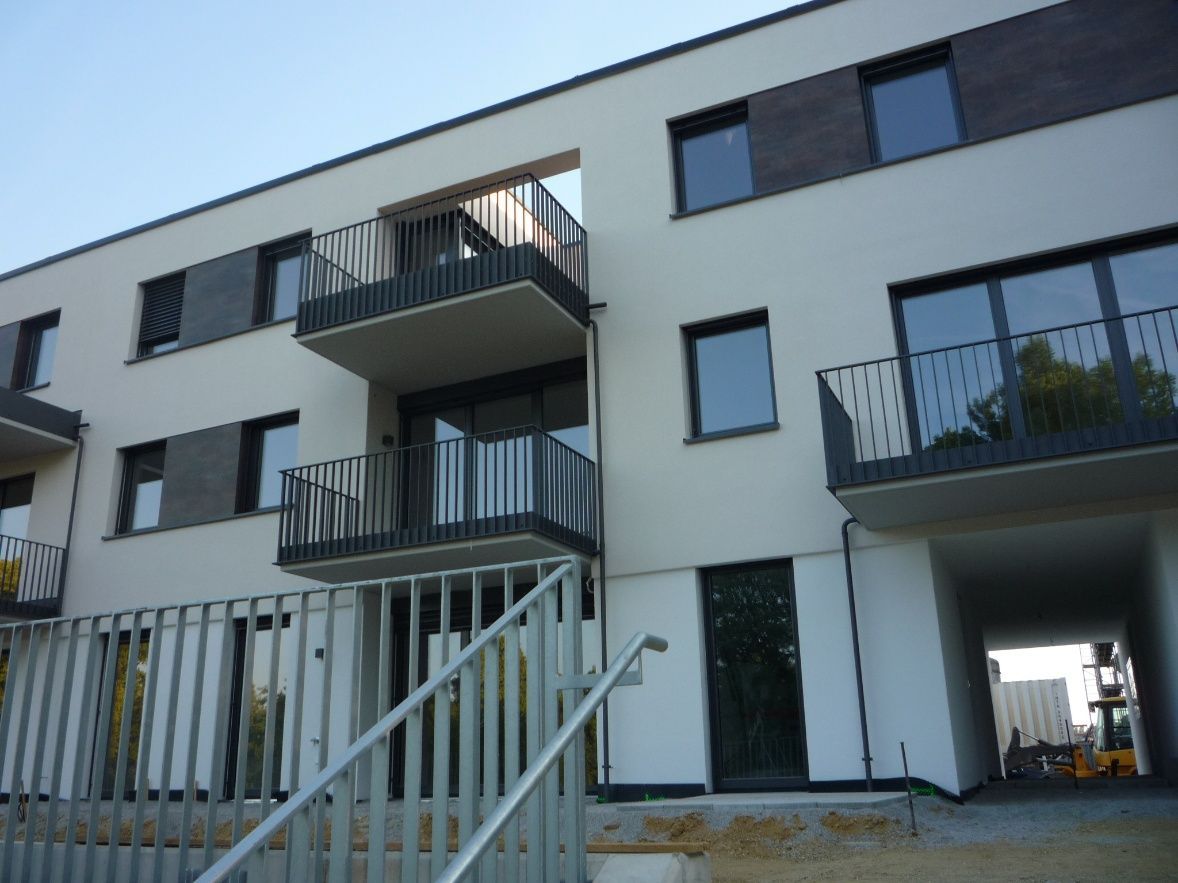 Modernes Mehrfamilienhaus mit weißer und dunkelgrauer Fassade, Balkonen und Metallgeländern.