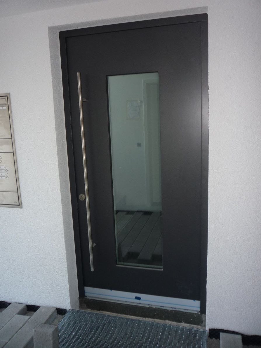 Dunkelgraue Haustür mit senkrechter Glasplatte, Edelstahlgriff, weiße Wände.