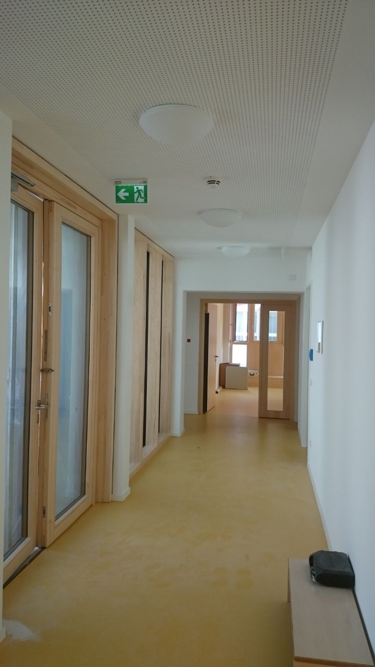 Flur mit gelbem Boden, weißen Wänden, Holztüren und einem Ausgangsschild.