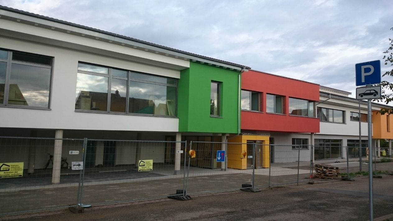 Buntes Schulgebäude im Bau mit Parkschild.
