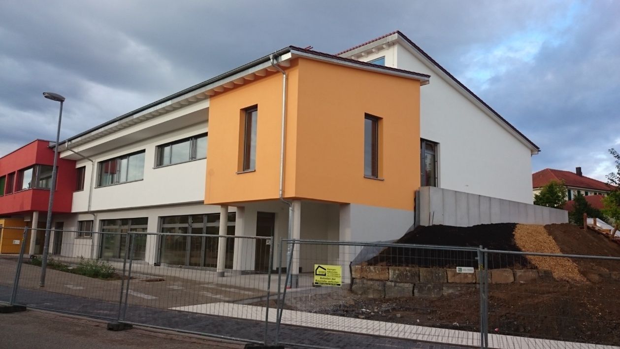 Gebäude mit roten, orangefarbenen und weißen Abschnitten; im Bau, eingezäuntes Gelände, bedeckter Himmel.