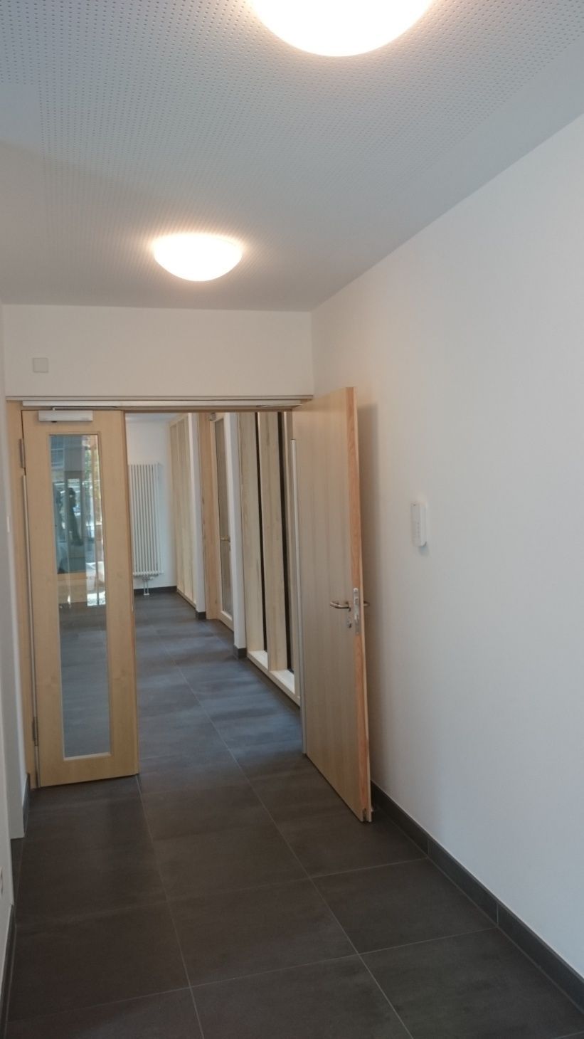 Flur mit dunkelgrauen Bodenfliesen, hellen Holztüren und weißen Wänden.