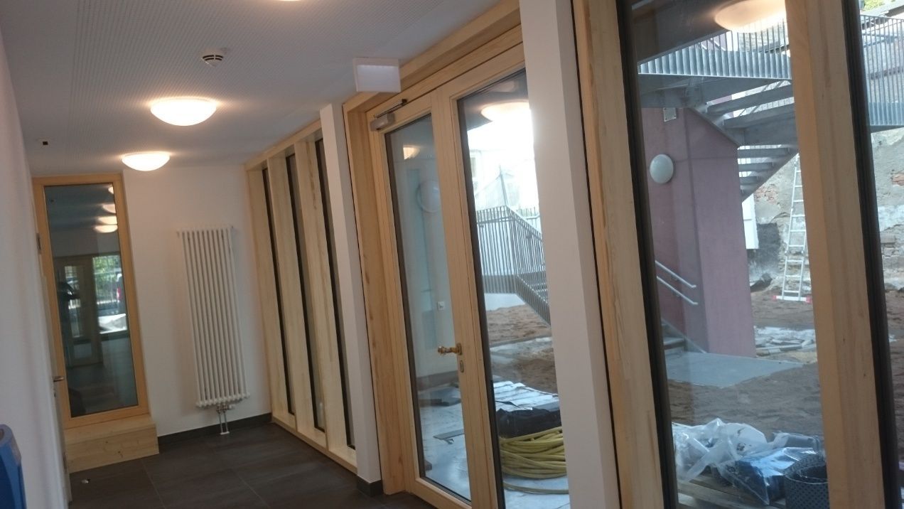 Innenflur mit großen Holzrahmenfenstern, Heizkörper und Beleuchtung.