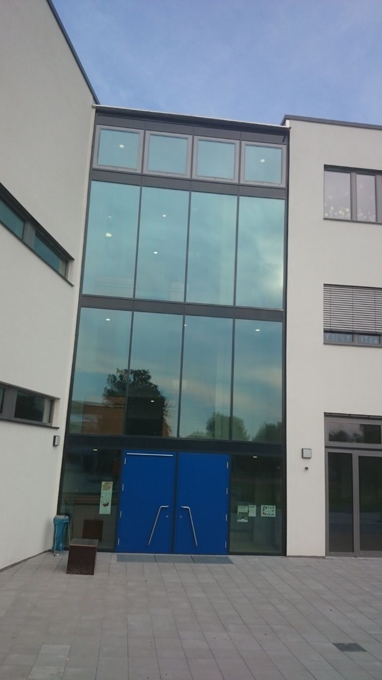 Außenansicht eines modernen Gebäudes mit einer blauen Tür und großen Glasfenstern. Bewölkter Himmel.