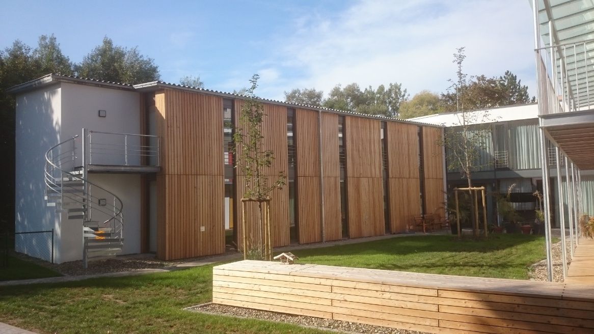 Gebäude mit Holzlamellenfassade, Wendeltreppe und Gründach. Sonniger Tag.
