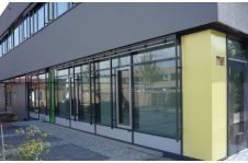 Modernes Gebäudeäußeres mit einer Reihe großer Fenster; gelbe und graue Akzente.