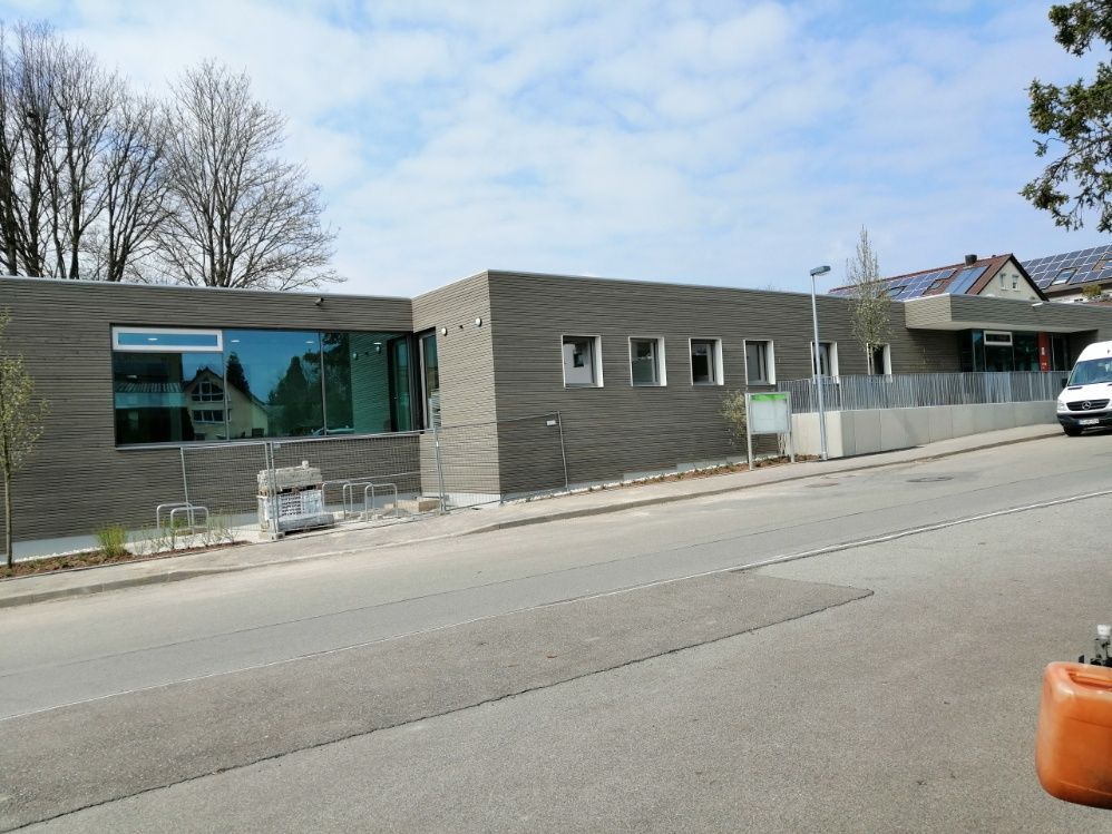 Modernes Gebäude mit grauer Holzverkleidung, großen Fenstern und einer Straße davor.