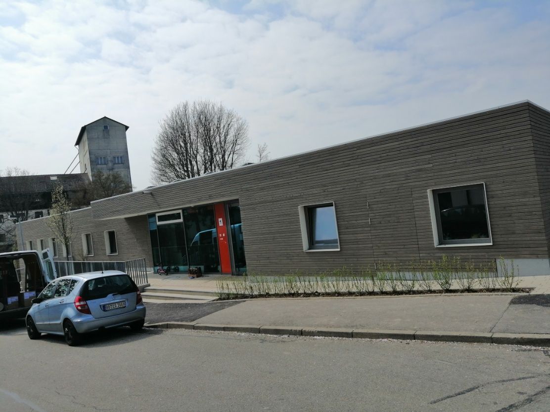 Ein modernes Gebäude mit schrägem Dach, davor parkt ein hellblaues Auto.